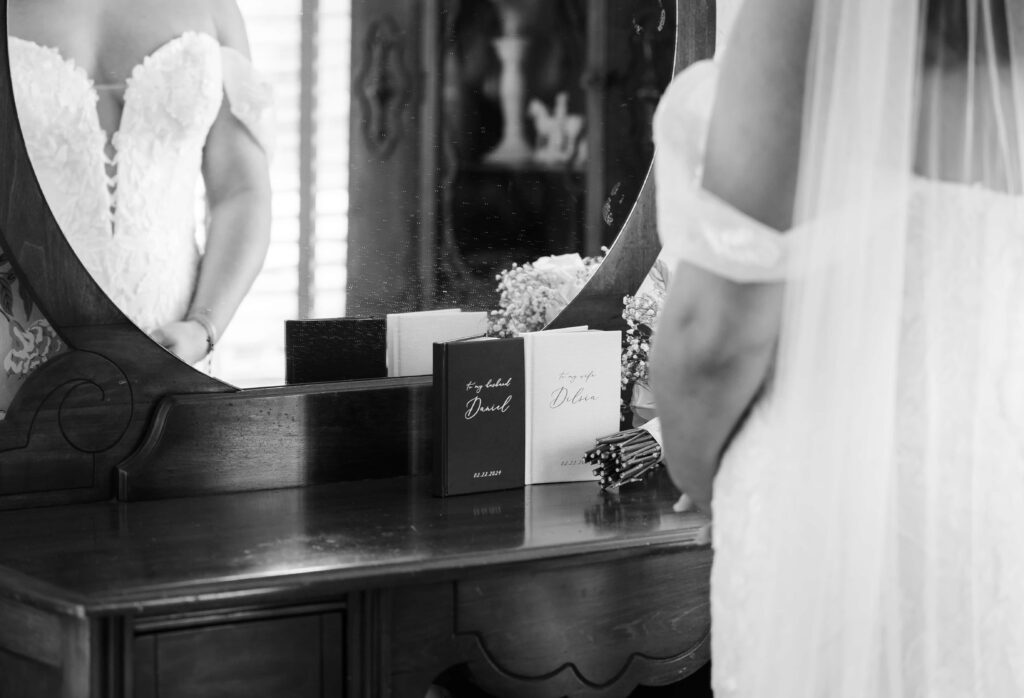 The Highland Manor Apopka - An intimate shot of the bride standing in front of the mirror, and the vow books are standing on the vanity | Wedding Photos by Phavy Photography - Apopka Wedding Photographer