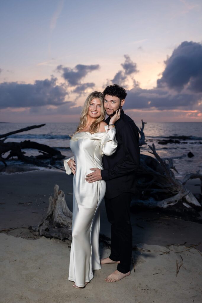 Couple posing barefoot on Driftwood Beach at sunrise in formal engagement attire