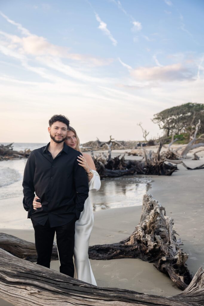 Couple posing on Driftwood Beach during engagement session with ocean and fallen trees in background