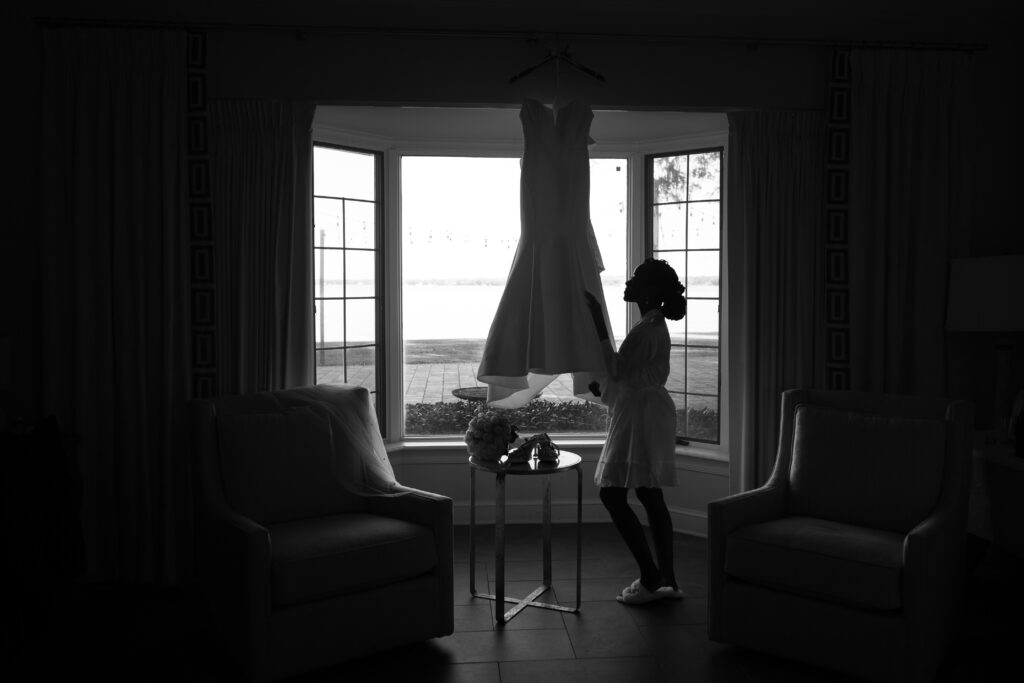 Bride in robe admiring her wedding dress in front of bay window at Azaleana Manor, Orange Park, FL