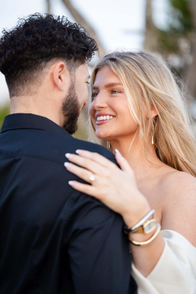 Bride-to-be’s hand showing solitaire ring while embracing fiancé at Jekyll Island engagement session