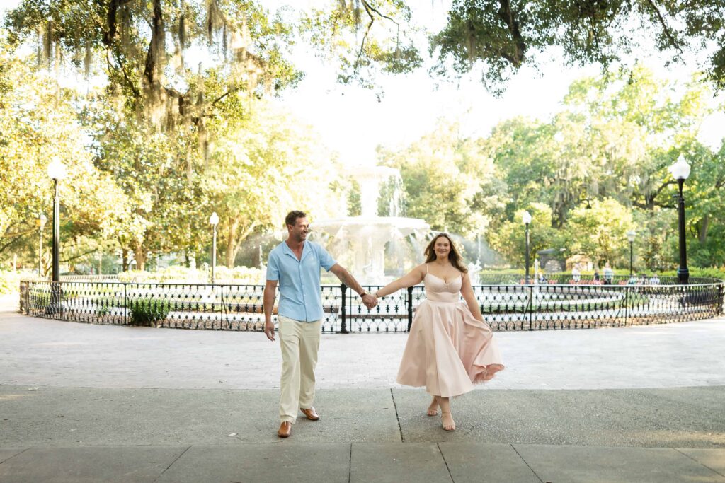 Newly engaged couple walking through Forsyth Park under Spanish moss